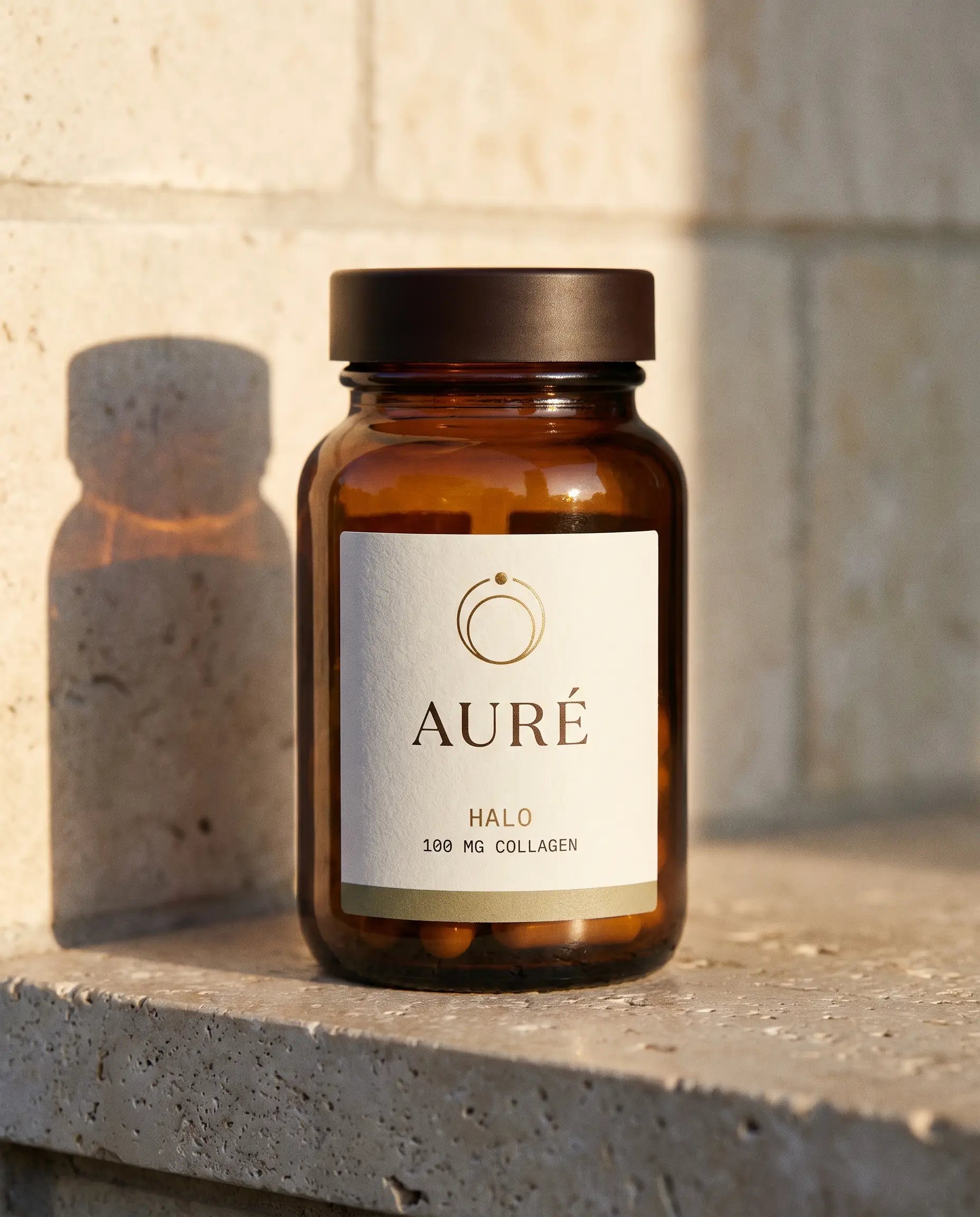 AURÉ Halo — honey-amber glass bottle, cream label printed with 100 mg collagen
